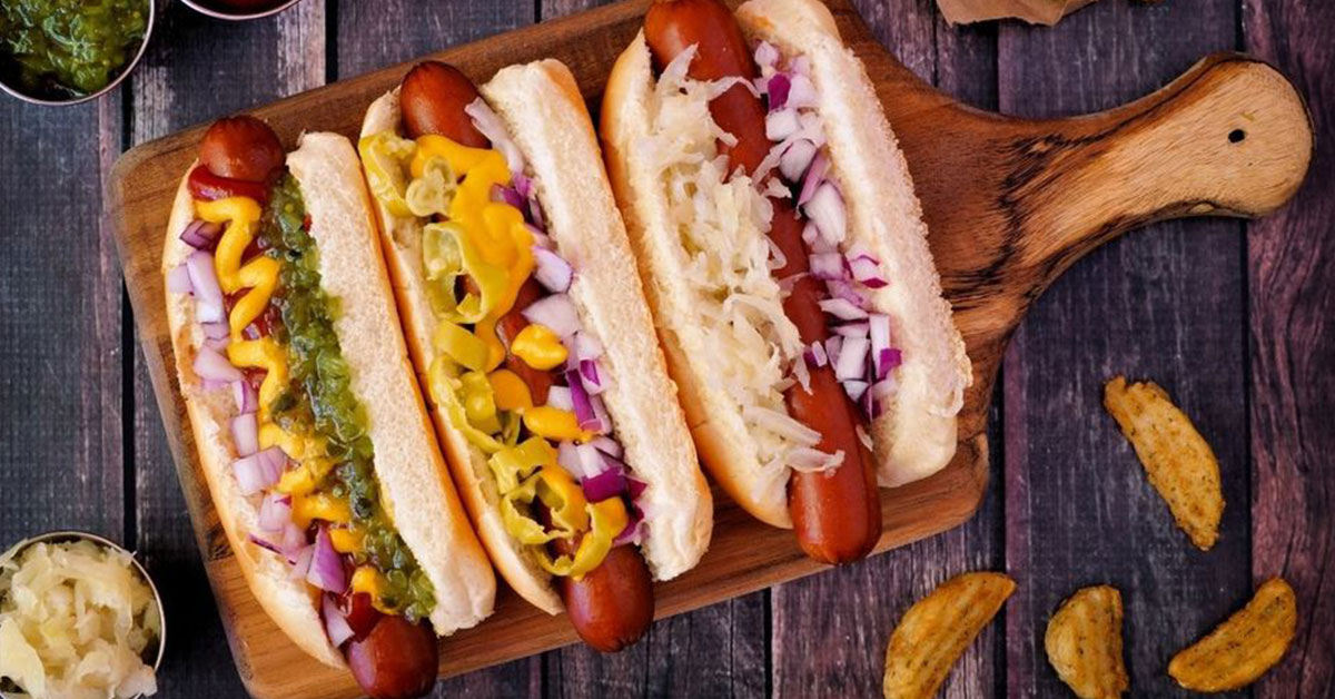 Three hot dogs with onions and different toppings served on a wooden platter