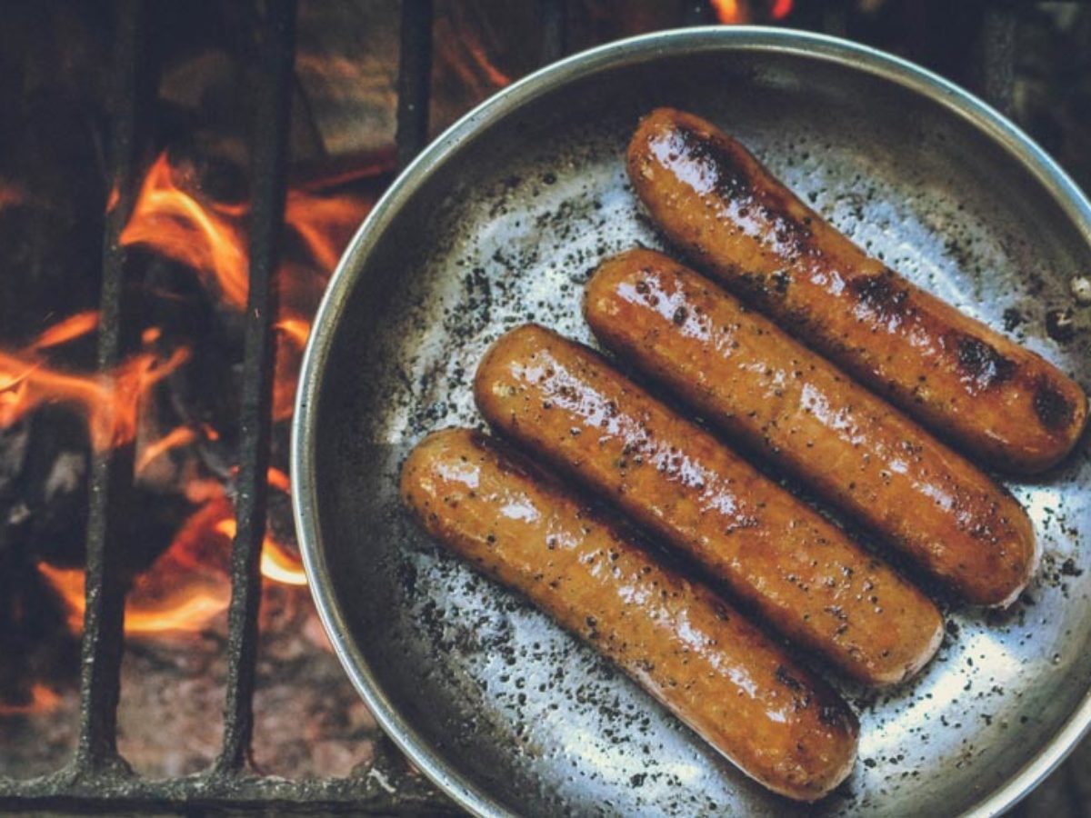 Four sumptuous-looking hot dogs in a frying pan above naked flames