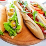 Hot dogs fully loaded with assorted toppings on a tray. Food background.