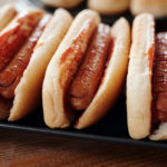 Hotdog sandwiches on black tray.