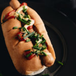 Hot dog and Vegetable on black ceramic plate.